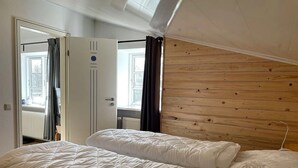 A bedroom with a wooden slat headboard, a large bed with white bedding, and a door leading to another room. - Vacation apartment Seeblick - Lindenhof (Steinberg)
