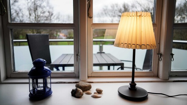 A table lamp with a wooden shade on a windowsill, a blue lantern, and a few stones. - Vacation apartment Seeblick - Lindenhof (Steinberg)