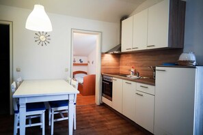 Cocina compacta con armarios blancos, encimera de madera y lámpara colgante.