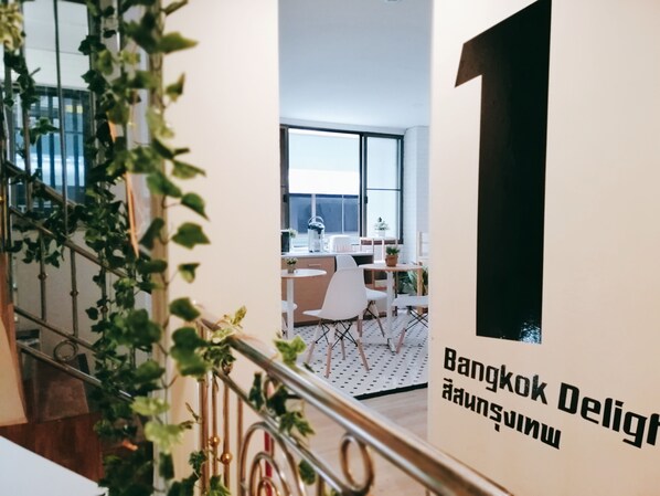 A modern interior with a staircase, a dining area, and a sign reading "Bangkok Delight". - White House Hostel (Bangkok)