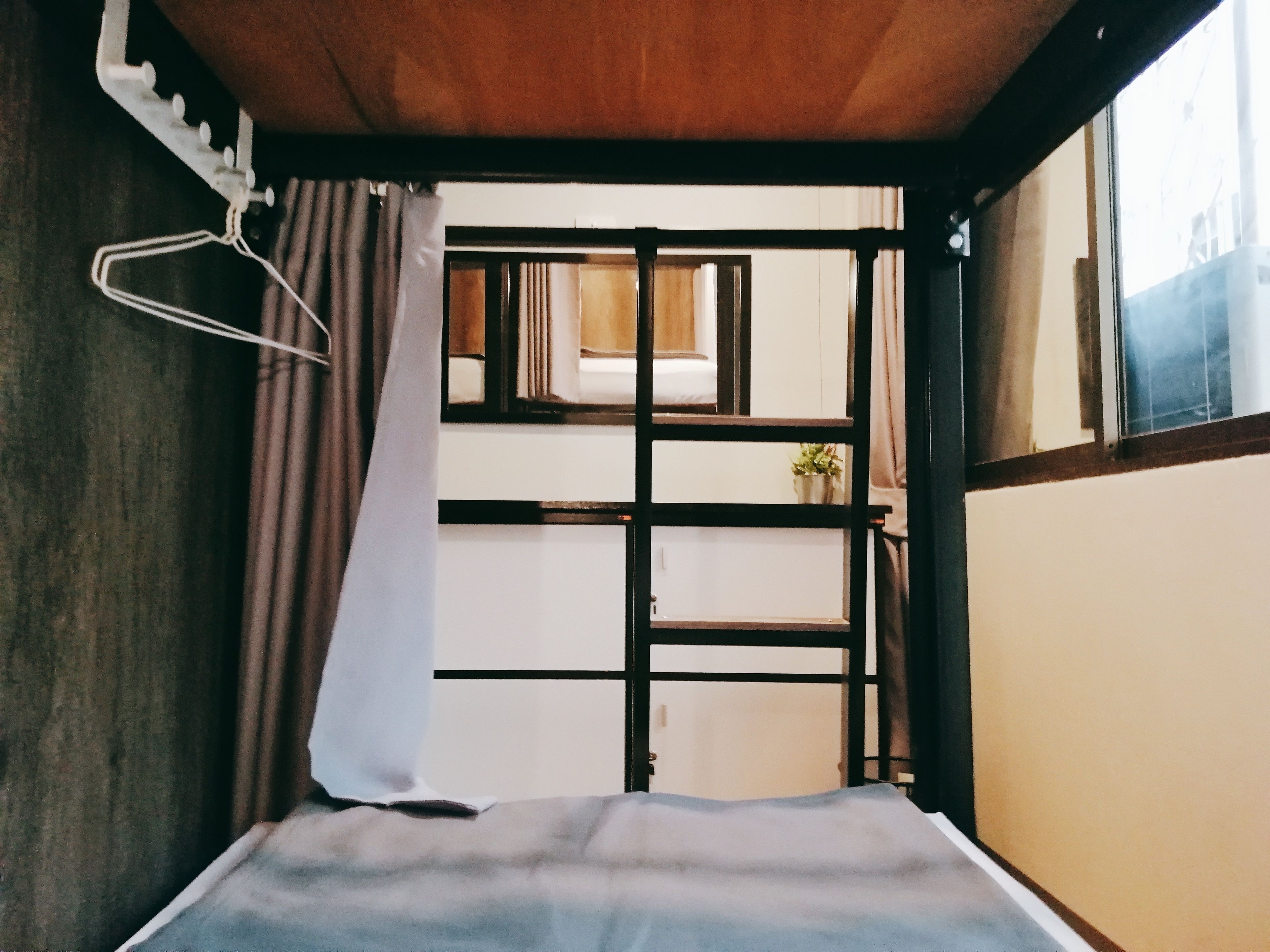 Un lit superposé avec une tête de lit en bois, une lampe suspendue et une fenêtre avec des rideaux.
