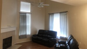 A living room with a fireplace, two windows with blinds, a ceiling fan, and a black leather sofa. - Fetokai Suite Inn, this is a beautiful home and suites with your vacation (Arlington)