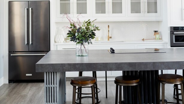 Una cocina moderna con armarios blancos, un refrigerador de acero inoxidable, una isla central con taburetes y una lámpara colgante.