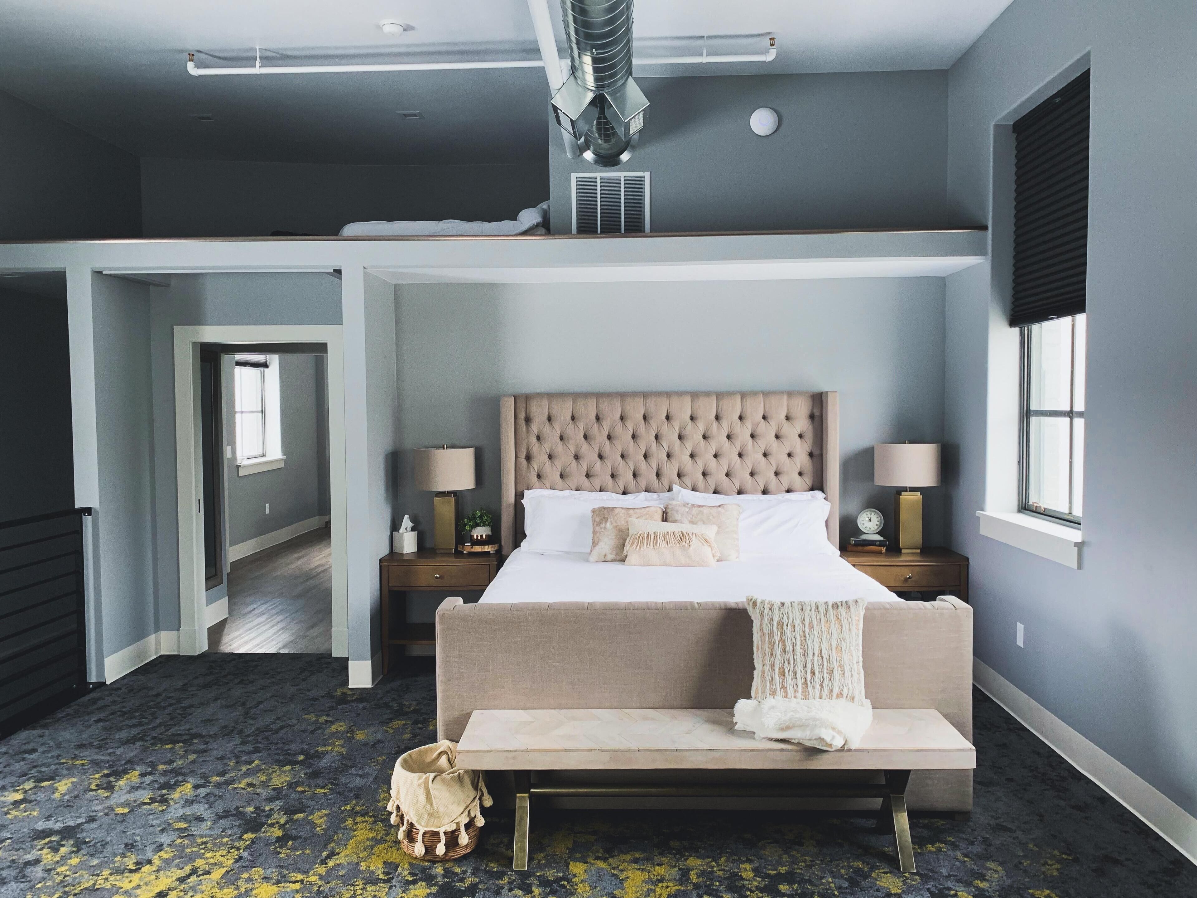A bedroom with a large bed, bedside tables, a bench, a window, and a ceiling vent.