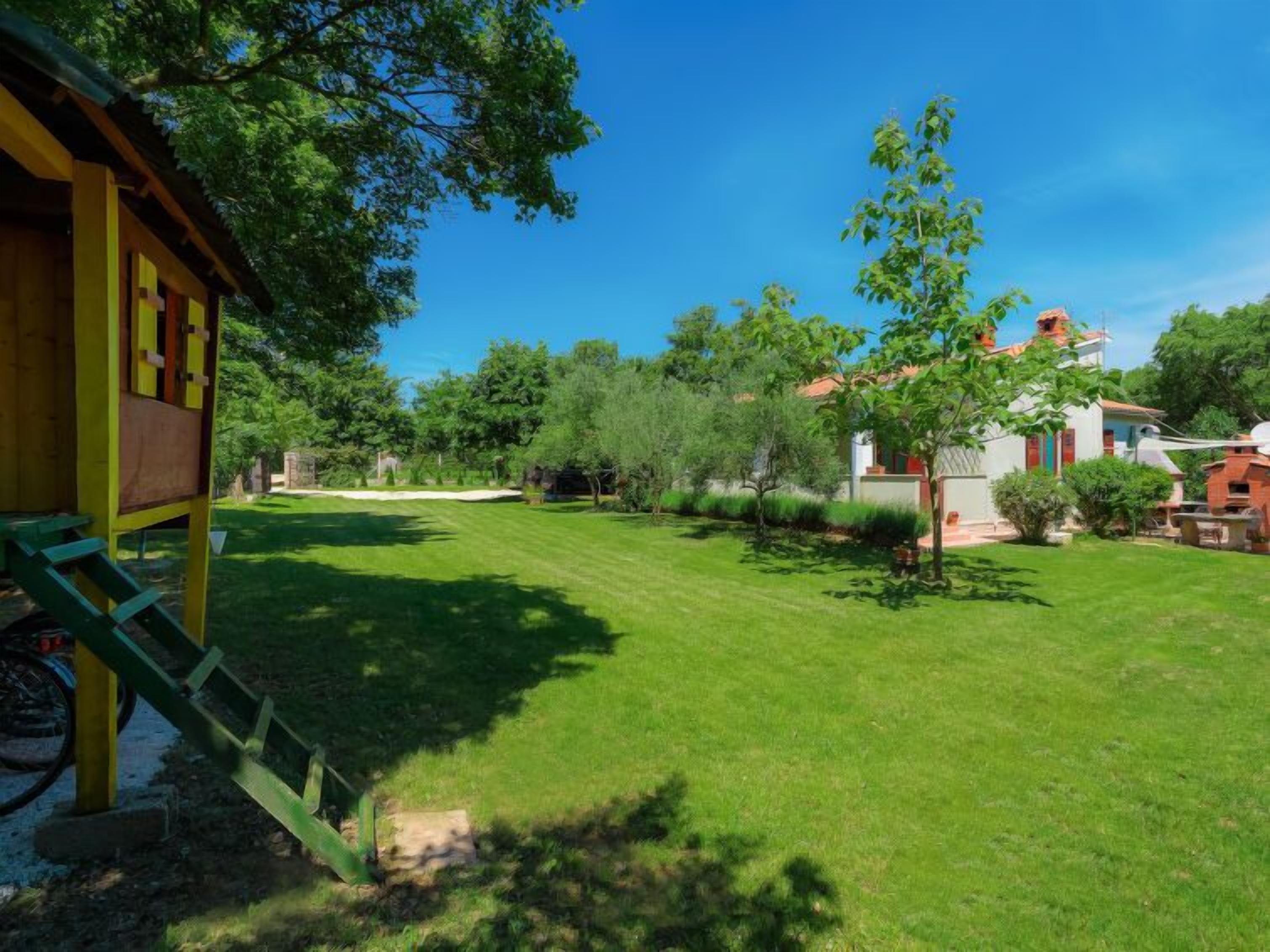 A well-maintained lawn with a play structure, surrounded by trees and a building with a red roof.