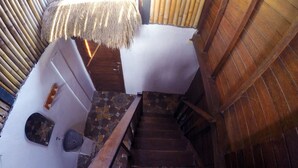 Un escalier en bois mène à une pièce dotée d’un toit de chaume et d’un plancher en pierre.