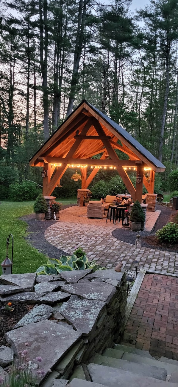 A wooden gazebo with string lights, outdoor furniture, and potted plants.