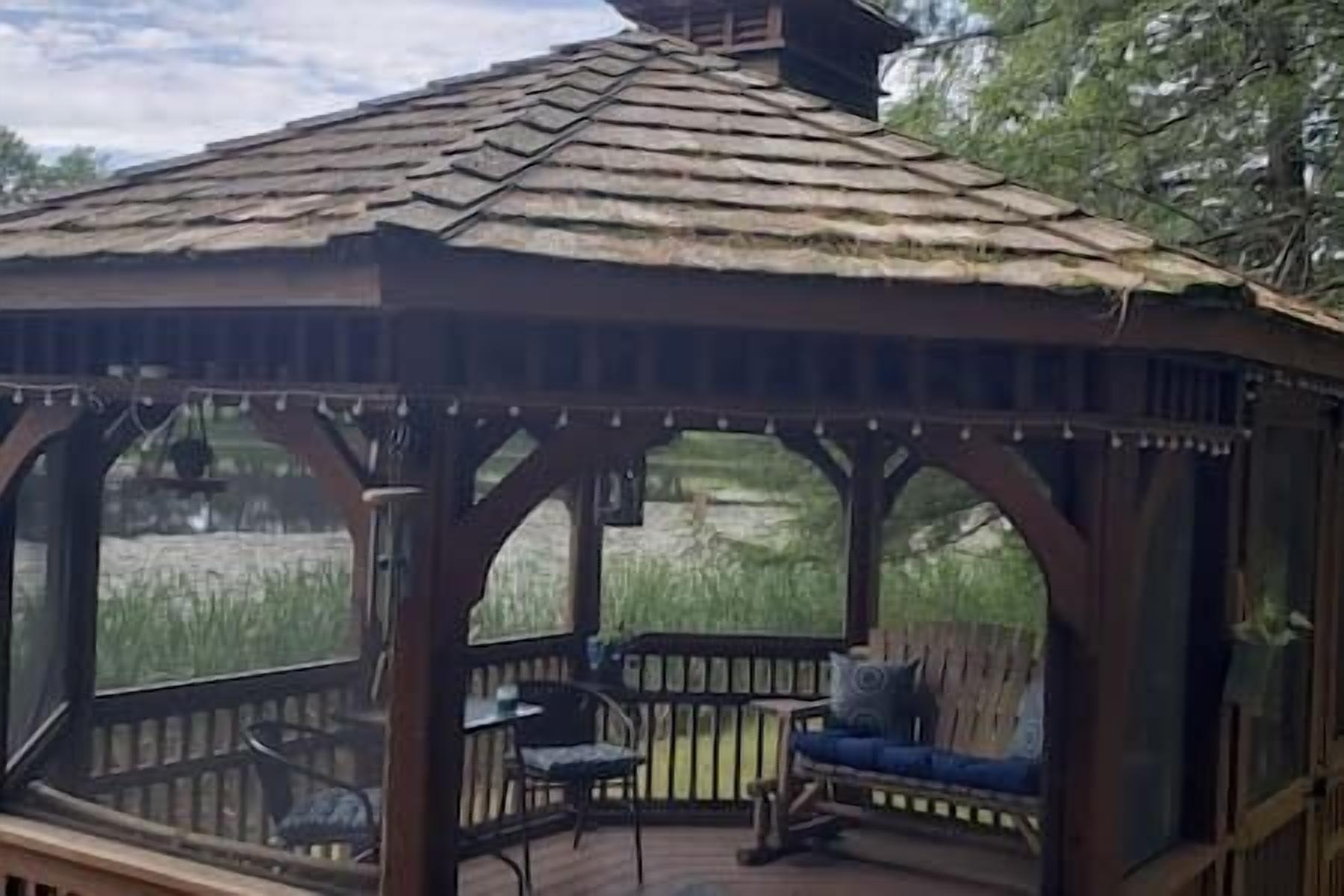 A wooden gazebo with a thatched roof, built-in benches, and a view of a natural landscape.