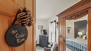 Une chambre comprenant un lit, une commode, un téléviseur et une porte sur laquelle est apposée une plaque indiquant : « La chambre des cèdres ».
