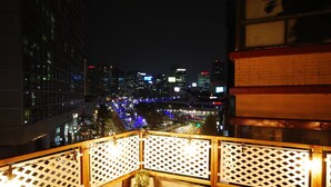 Vista noturna da cidade a partir de uma varanda com grade de treliça e planta em vaso.