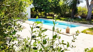 Une piscine entourée de verdure, avec un bâtiment blanc en arrière-plan.