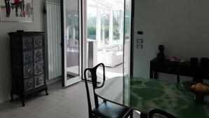 Une porte-fenêtre coulissante donne sur un balcon où se trouvent une chaise et une table d’extérieur, toutes deux de couleur blanche.