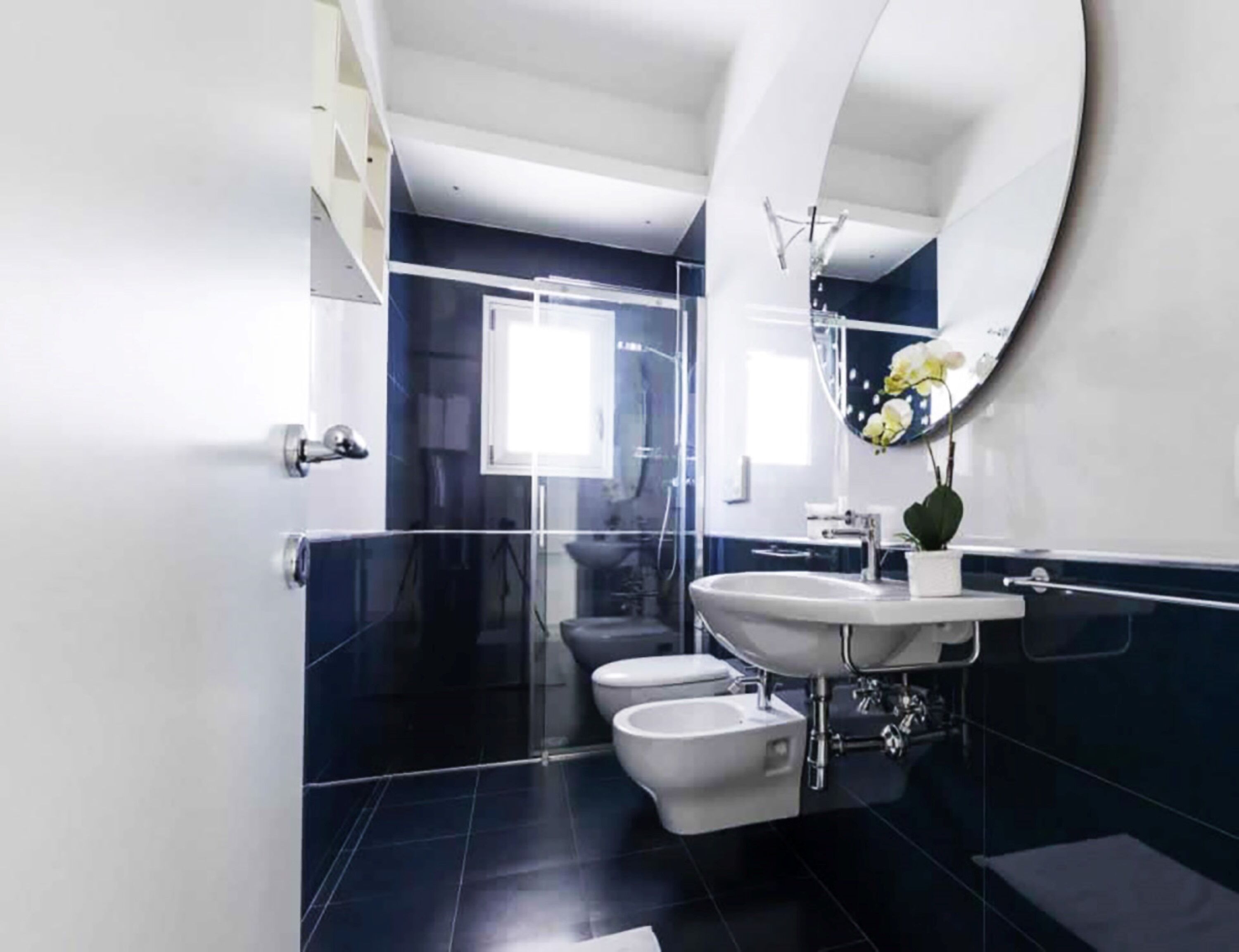 A modern bathroom with a large mirror, a sink, two toilets, and a shower area.