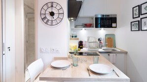 A modern kitchen with a wooden dining table, white chairs, a black clock, and a microwave. - Le Petit Botté - Studio plein cœur de Rennes (Rennes)