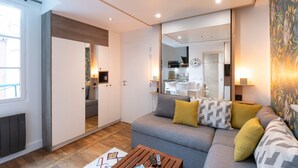 A modern living room with a grey sofa, yellow and patterned cushions, a wooden coffee table, and a large mirror reflecting the kitchen area. - Le Petit Botté - Studio plein cœur de Rennes (Rennes)