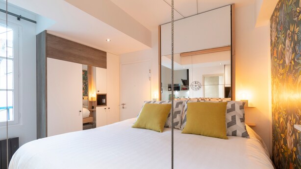 A modern bedroom with a large bed, a mirror, and a view of the kitchen. - Le Petit Botté - Studio plein cœur de Rennes (Rennes)