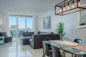 A modern living room with a glass dining table, leather sofas, and a large window with a city view.