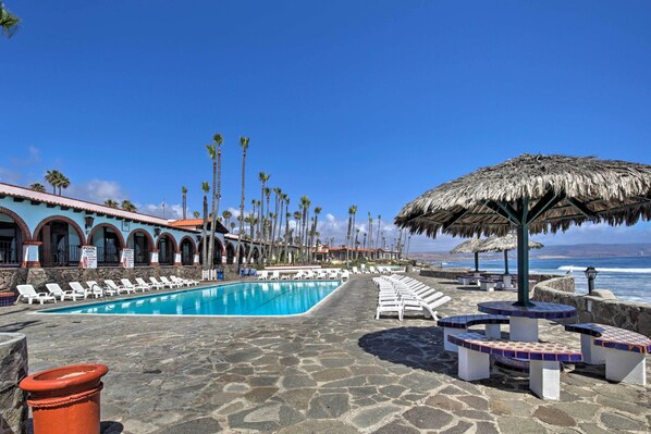 A pool area with lounge chairs and umbrellas, a stone pathway, and a building with arched windows.