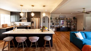 Uma cozinha moderna com uma ilha grande, banquetas, eletrodomésticos de aço inoxidável e iluminação pendente.