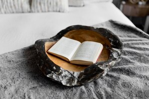 Un libro sobre un cuenco de madera sobre una cama con una manta gris.