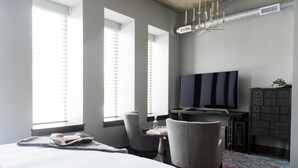 A modern hotel room with a large bed, a desk with a flat-screen TV, a chair, and a dresser.