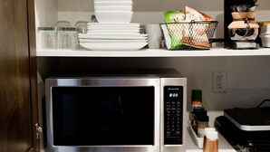 A kitchen with a microwave, a coffee maker, and shelves with dishes and containers.