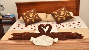 A neatly made bed with a heart-shaped towel arrangement, decorative pillows, and rose petals scattered on the bed. - New York Guest House (Negombo)