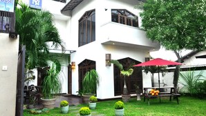 A two-story building with a white exterior, large windows, and a red umbrella in the courtyard. - New York Guest House (Negombo)