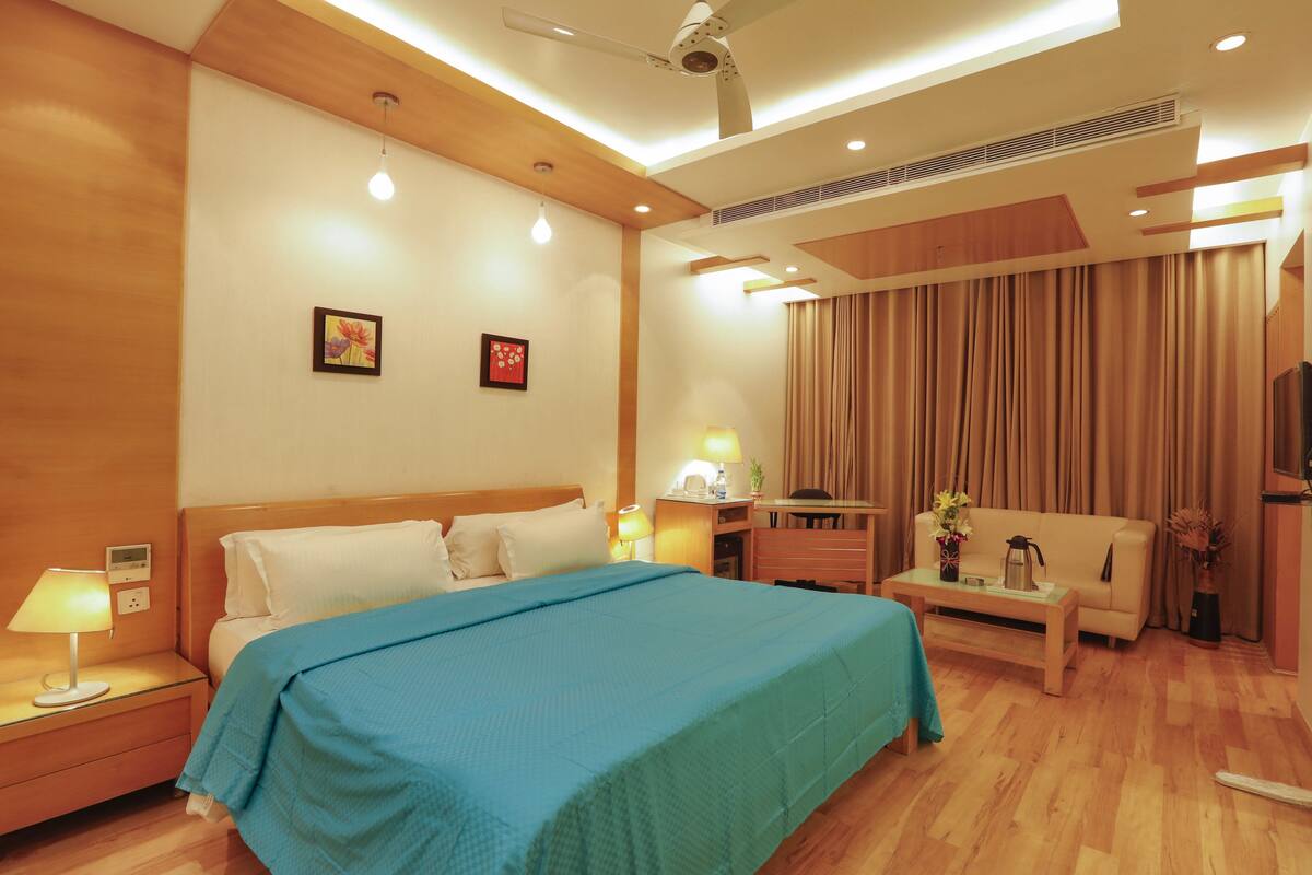 Quarto de hotel com cama, mesa de cabeceira, luminária e um sofá.