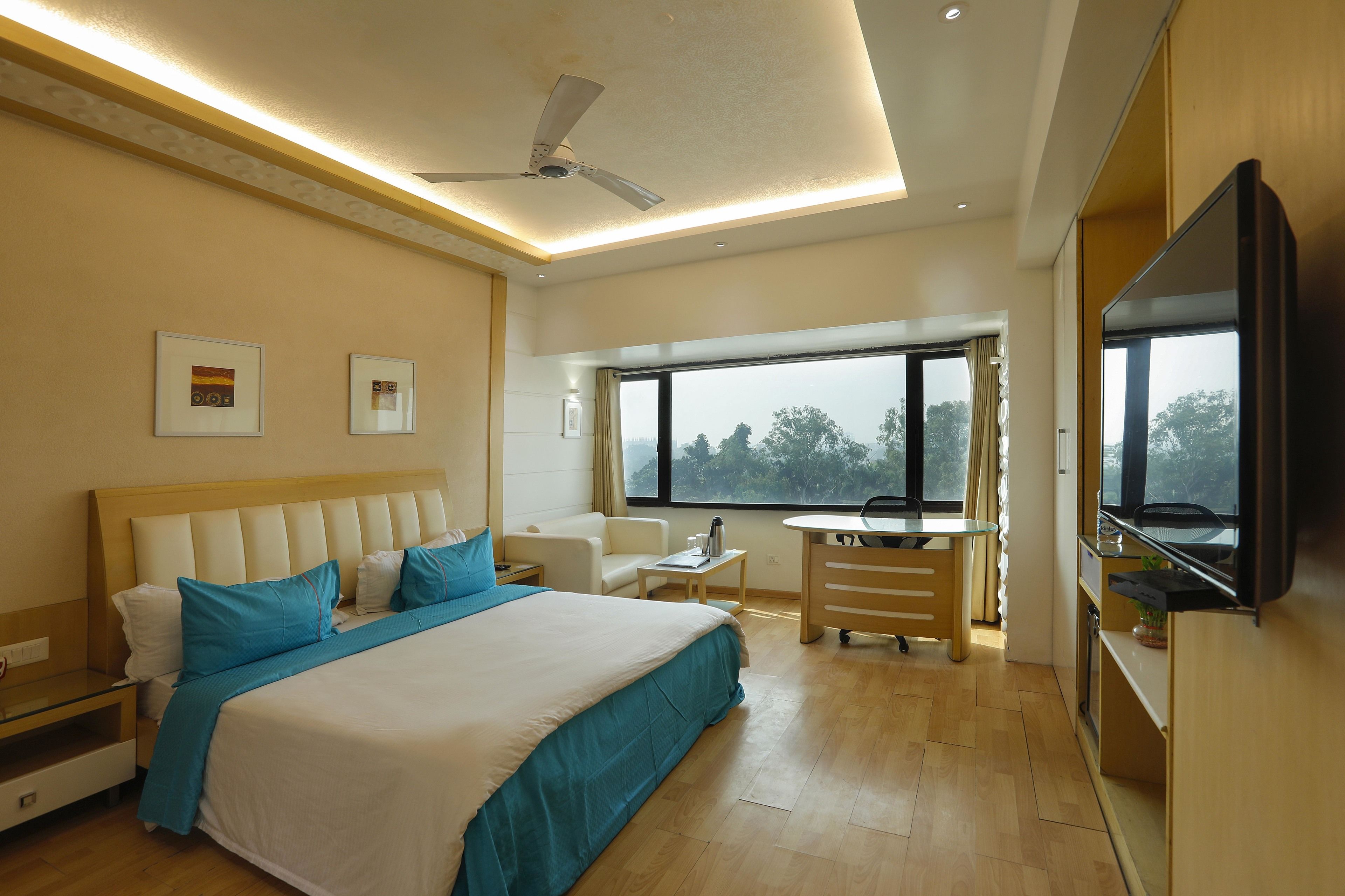 Ein Hotelzimmer mit einem großen Bett, einem Schreibtisch, einem Stuhl, einem Fernseher und einem Deckenventilator.