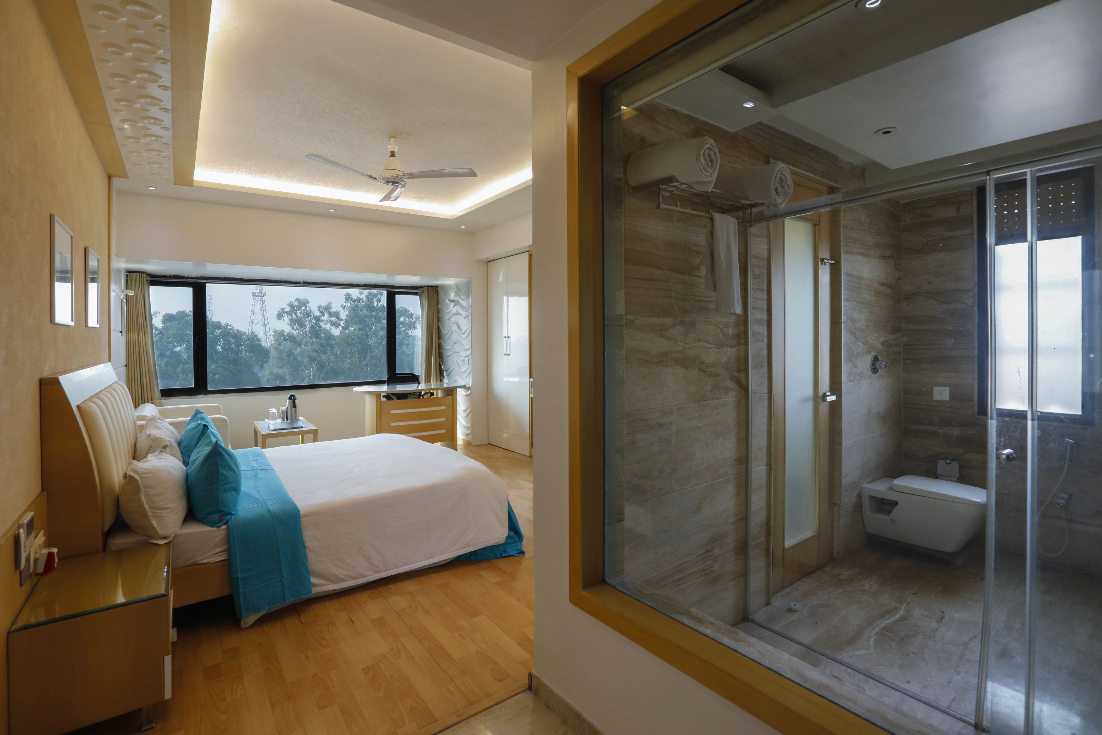 A modern bedroom with a large bed, bedside tables, a desk, and a window with a view of trees.