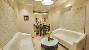 A modern living room with two white leather sofas, a round glass coffee table, and a dining area with a table and chairs. - Shivoy Hotel (Gorakhpur)
