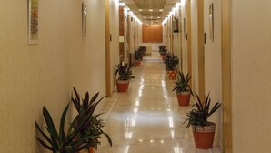 A hotel hallway with potted plants, doors, and ceiling lights. - Shivoy Hotel (Gorakhpur)