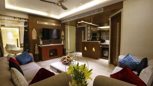 A modern living room with a sofa set, a flat-screen TV, a fireplace, and a kitchen area in the background. - Shivoy Hotel (Gorakhpur)