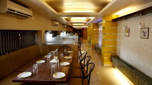A restaurant with a long wooden table set for dining, air conditioning units, and a modern interior design. - Shivoy Hotel (Gorakhpur)
