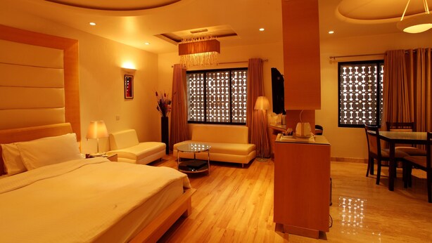 A hotel room with a large bed, a sofa, a desk, and a dining area. - Shivoy Hotel (Gorakhpur)