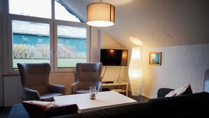 Una sala de estar acogedora con una mesa blanca, dos sillones, un sofá, un televisor y una lámpara.