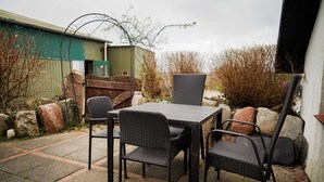 Un patio al aire libre con una mesa y sillas, rodeado de rocas y un edificio.
