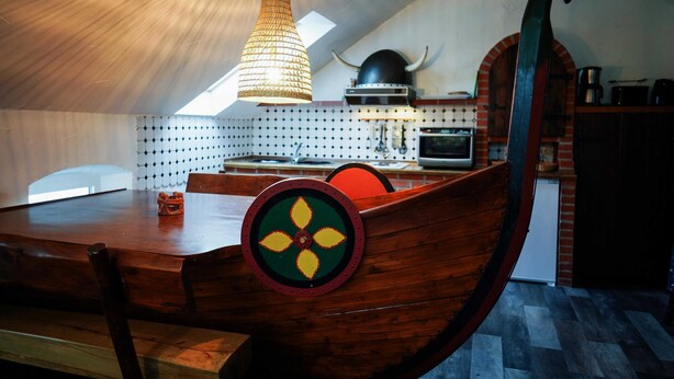 Comedor con una mesa con forma de barco de madera, una lámpara colgante y un horno de ladrillo al fondo.