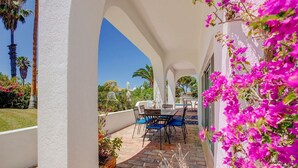 Una veranda coperta all'aperto con tavolo e sedie, circondata da pareti bianche e fiori di bouganvillea rosa.