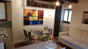 A dining area with a glass table and colorful chairs, a white sofa, and a bookshelf with books. - Oasi dei Vandali, small and cozy residence in the historic center, 5 min from the sea (Mondolfo)
