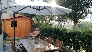 A wooden table with six chairs, a hanging chair, and a large umbrella providing shade. - Oasi dei Vandali, small and cozy residence in the historic center, 5 min from the sea (Mondolfo)