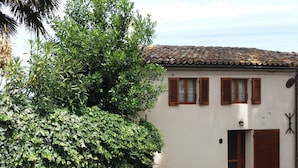 A white building with a tiled roof, wooden shutters, and a brick pathway leading to the entrance. - Oasi dei Vandali, small and cozy residence in the historic center, 5 min from the sea (Mondolfo)