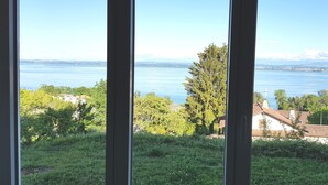 A view through window blinds of a lake with buildings and trees in the foreground. - Littoral Lac (La Grande-Béroche)