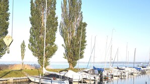 A marina with boats docked, surrounded by trees and calm water. - Littoral Lac (La Grande-Béroche)