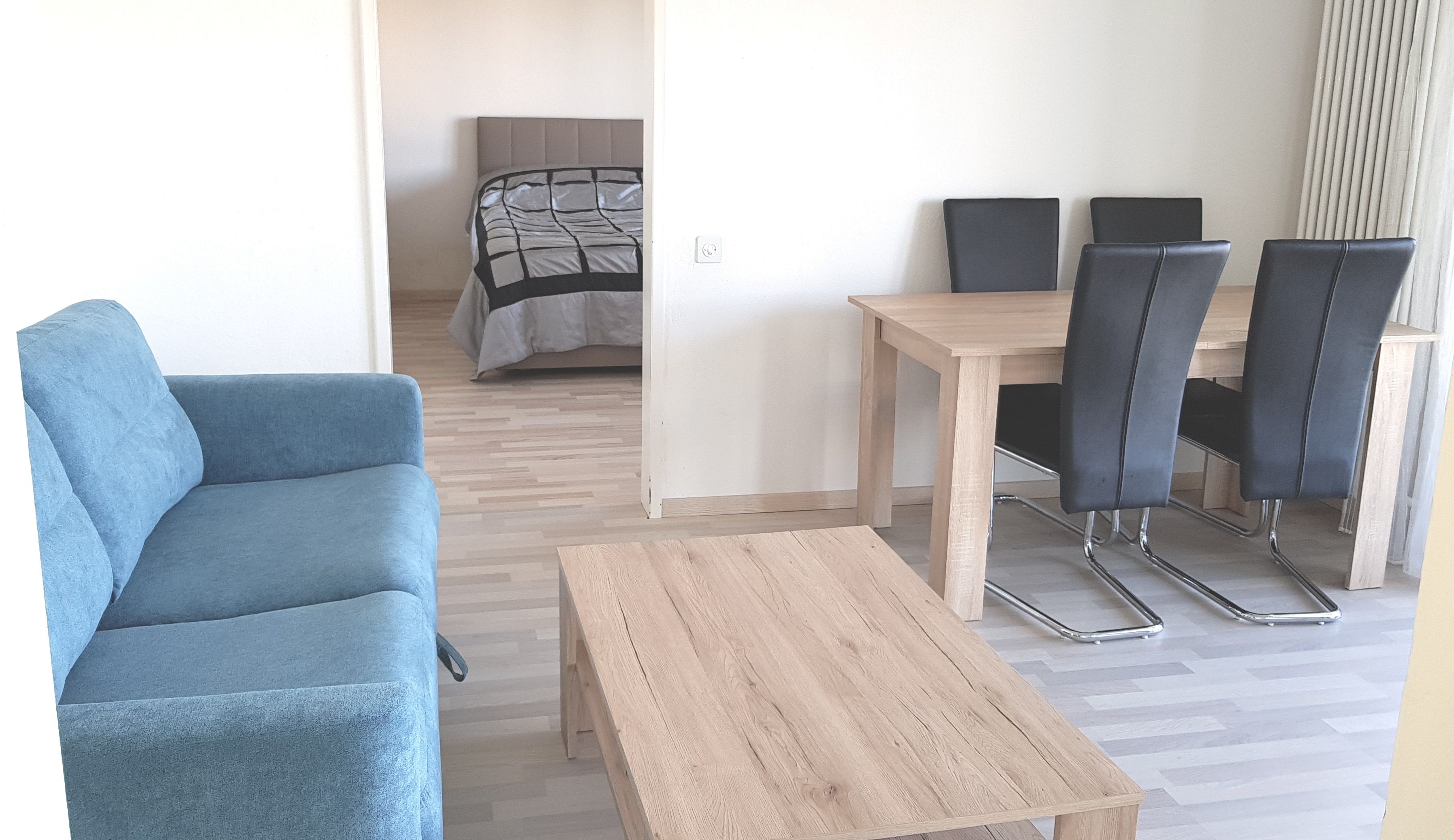 Una habitación moderna con un sillón azul, una mesa de madera y un comedor con cuatro sillas y una mesa.