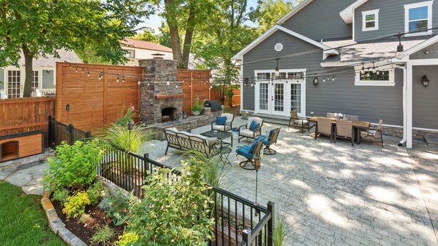 A backyard patio with a stone fireplace, outdoor furniture, and a brick patio.