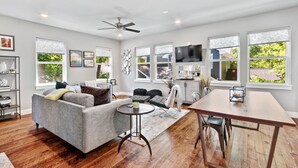 A spacious living room with a grey sofa, a round coffee table, a dining table with chairs, and a ceiling fan.