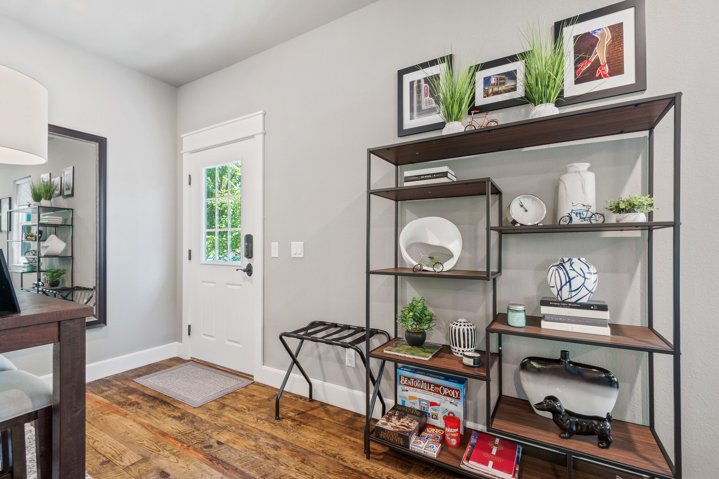 A modern living room with a wooden floor, a white door, and a bookshelf with various decorative items.