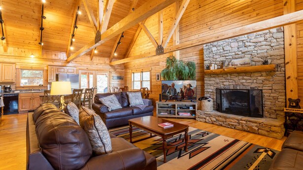 A spacious living room with a stone fireplace, leather sofas, and a television. - Waterfront Home in Picturesque Community (Jefferson)